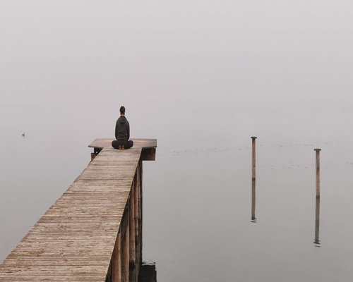 Person meditating by calm lake at sunset